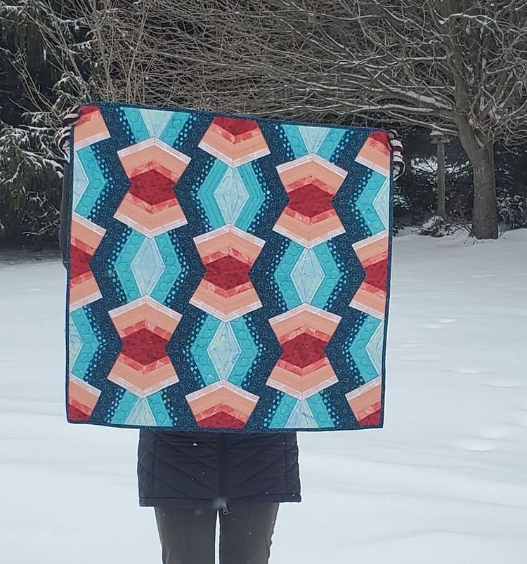 A pink and blue Bracken quilt is held by the maker outside in the snow.