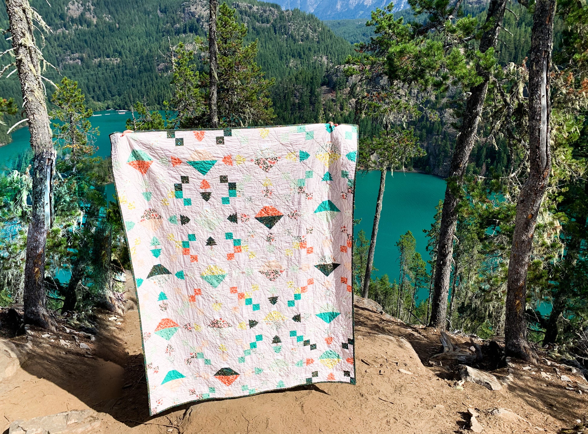 The Highline Quilt Pattern - Julia Wachs Designs - The Highline quilt being held in front of a bright blue lake.