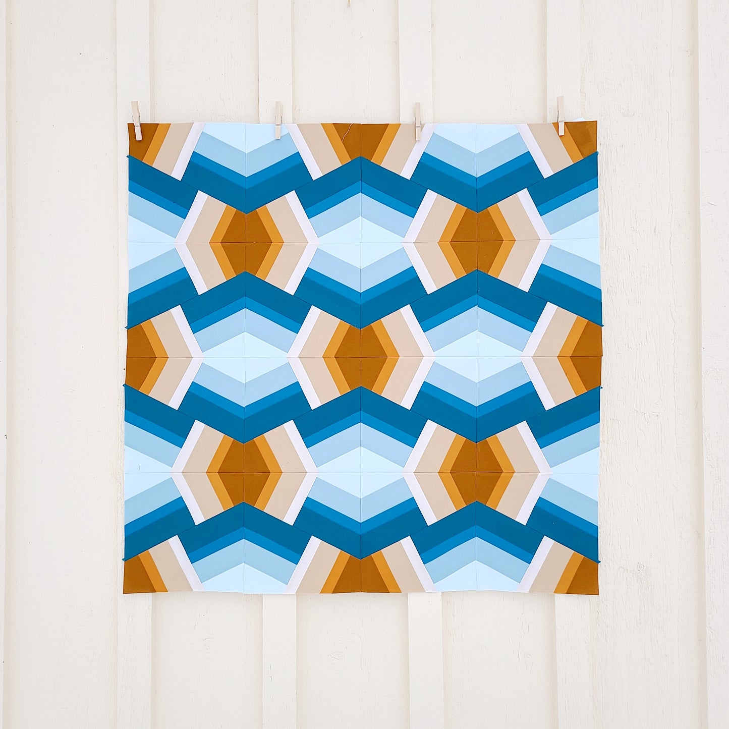 A blue and orange Bracken quilt hangs on a white wall.