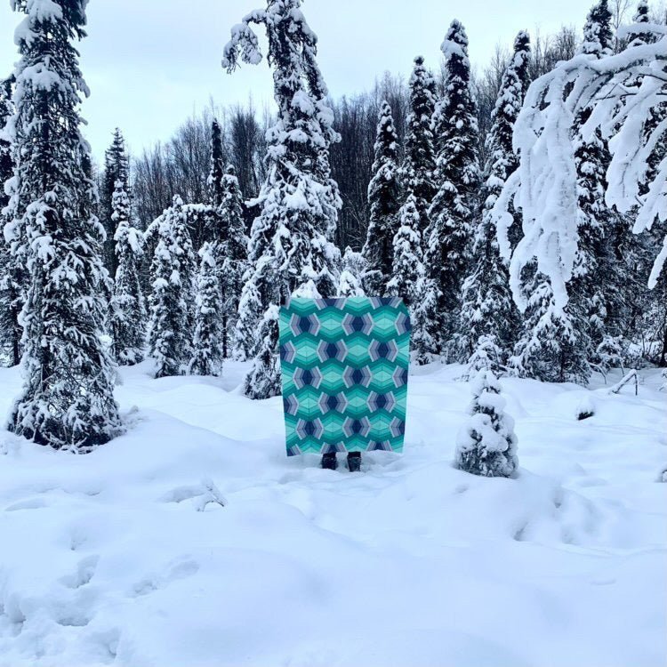 A teal and blue Bracken quilt is held by the maker outside in the snow.