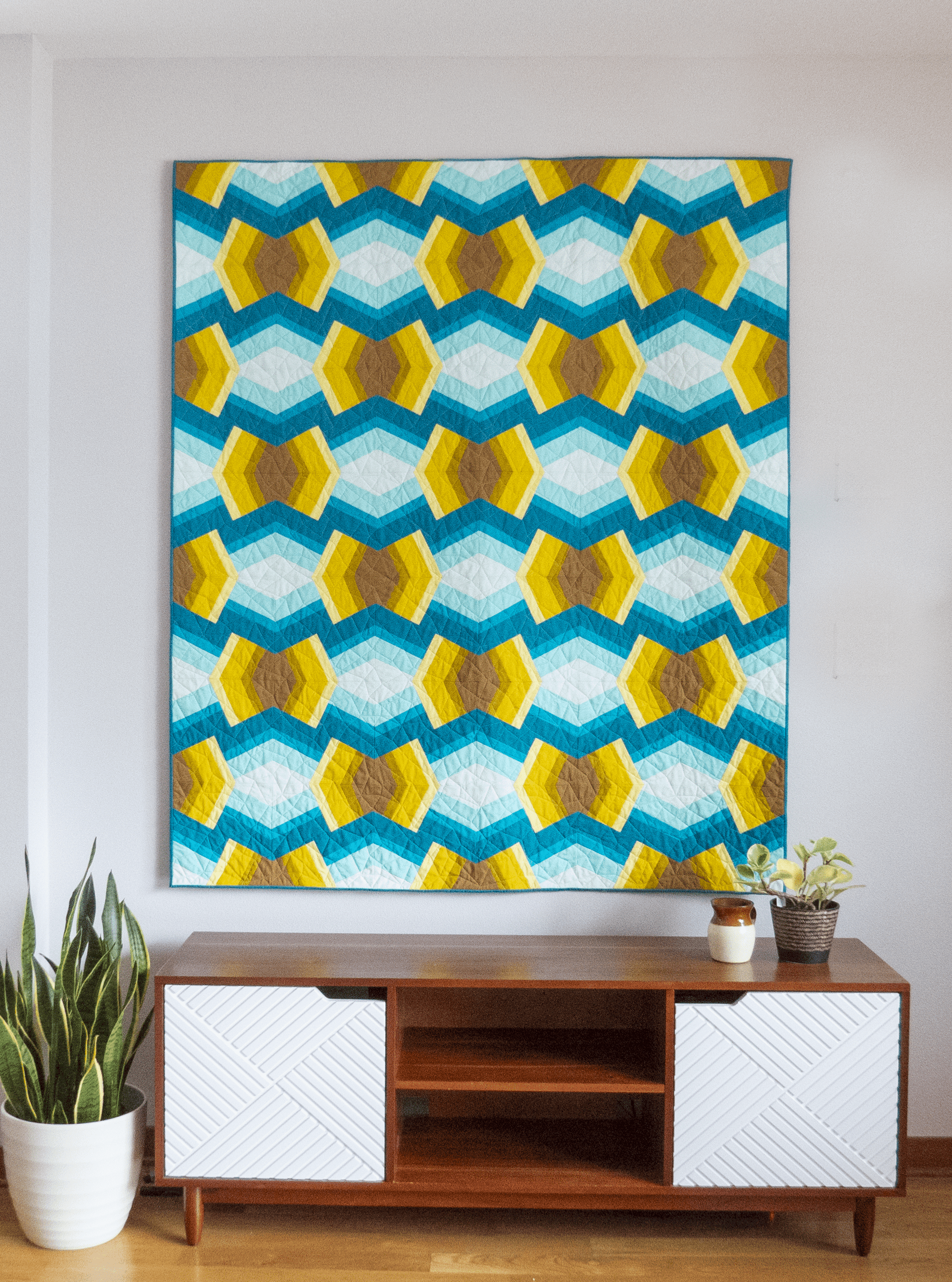 Bracken Quilt - Julia Wachs Designs - A teal and yellow Bracken quilt hangs on a gray wall.