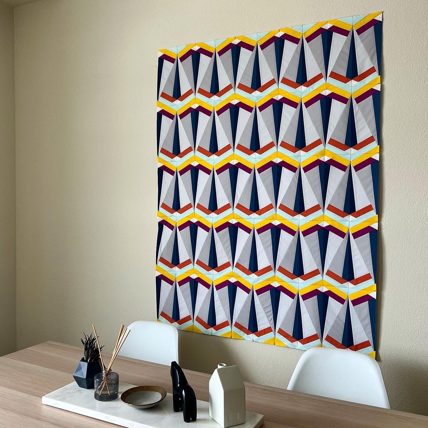 Skye Quilt Pattern - Julia Wachs Designs - A gray and yellow Skye quilt hung on a beige wall.