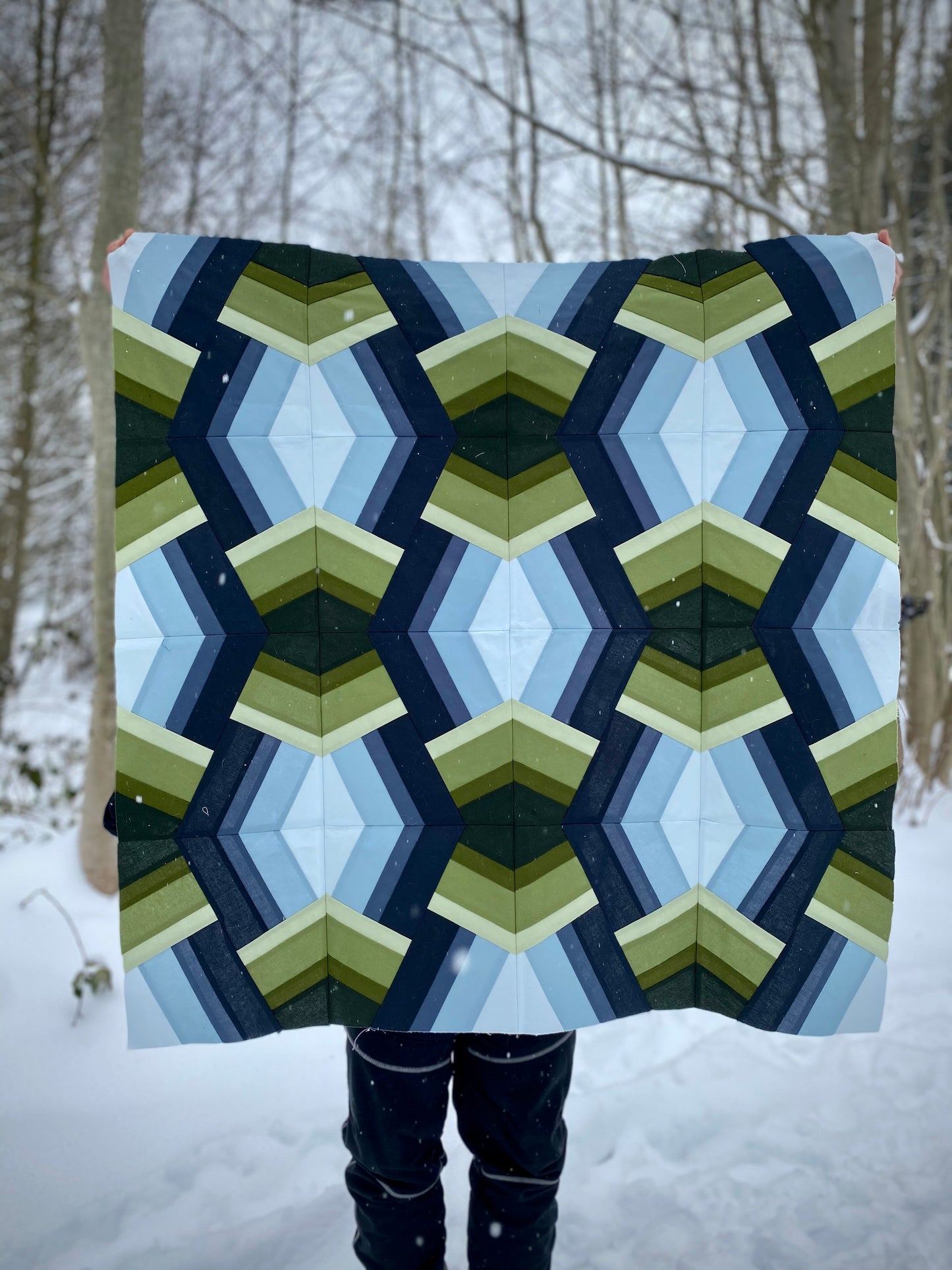 Bracken Quilt - Julia Wachs Designs - A blue and green Bracken quilt is held by its maker outside in the snow.